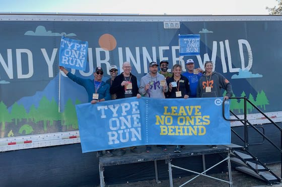 The Type One Run relay team, eight runners with banners and medals in front of the event trailer.