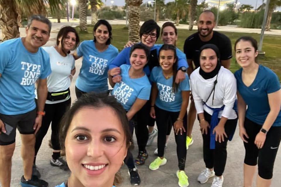A Type One Run group crowding into a selfie under palm trees after a run, everyone grinning.